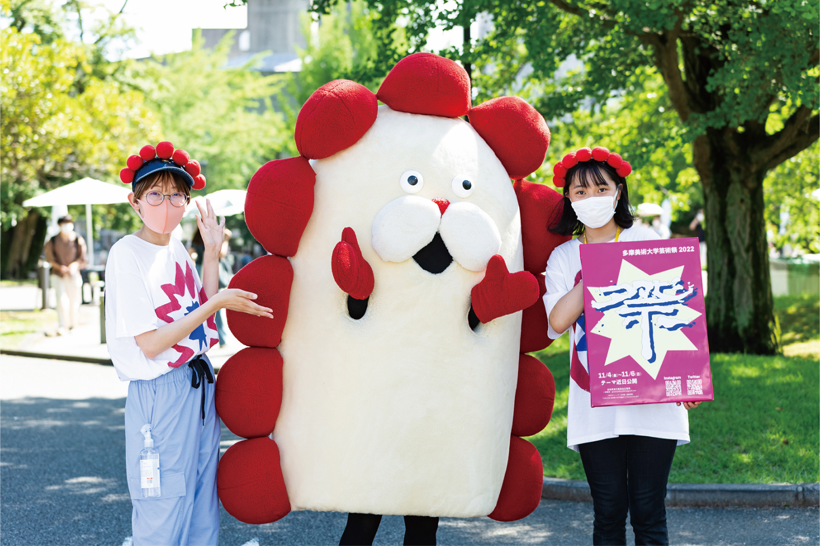 屋外イベントでキャラクターの着ぐるみとポスターを持つスタッフ二人。